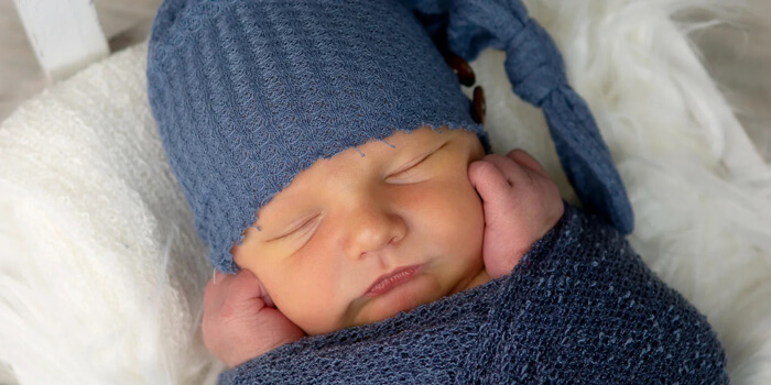 baby bundled in blue hat and blanket laying on white blanket